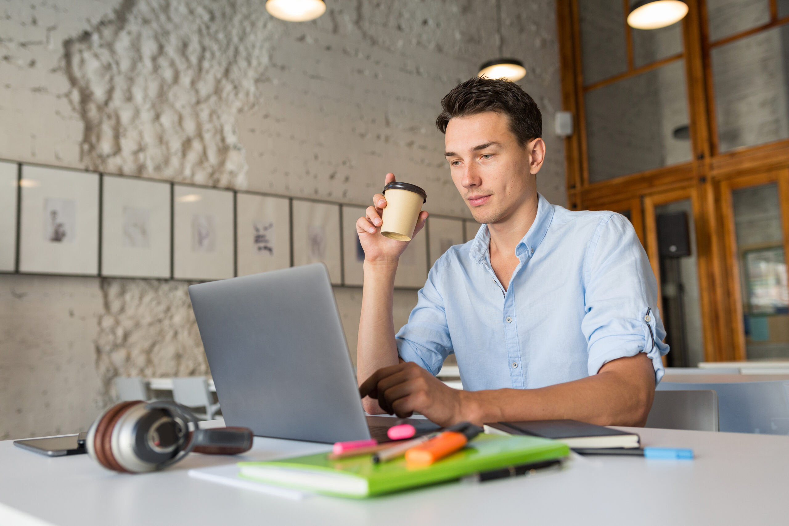 modern handsome man busy at his work drinking coffee, working on laptop in co-working office, young professional, concentration